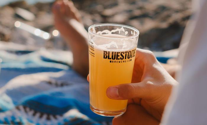 A hand is holding a half pint glass of beer, the sun is shining